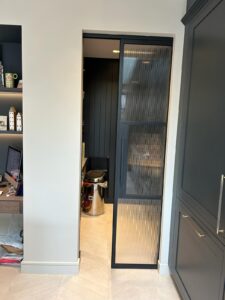 A stylish narrow passage featuring black-framed sliding doors internal with ribbed glass, providing a subtle separation.