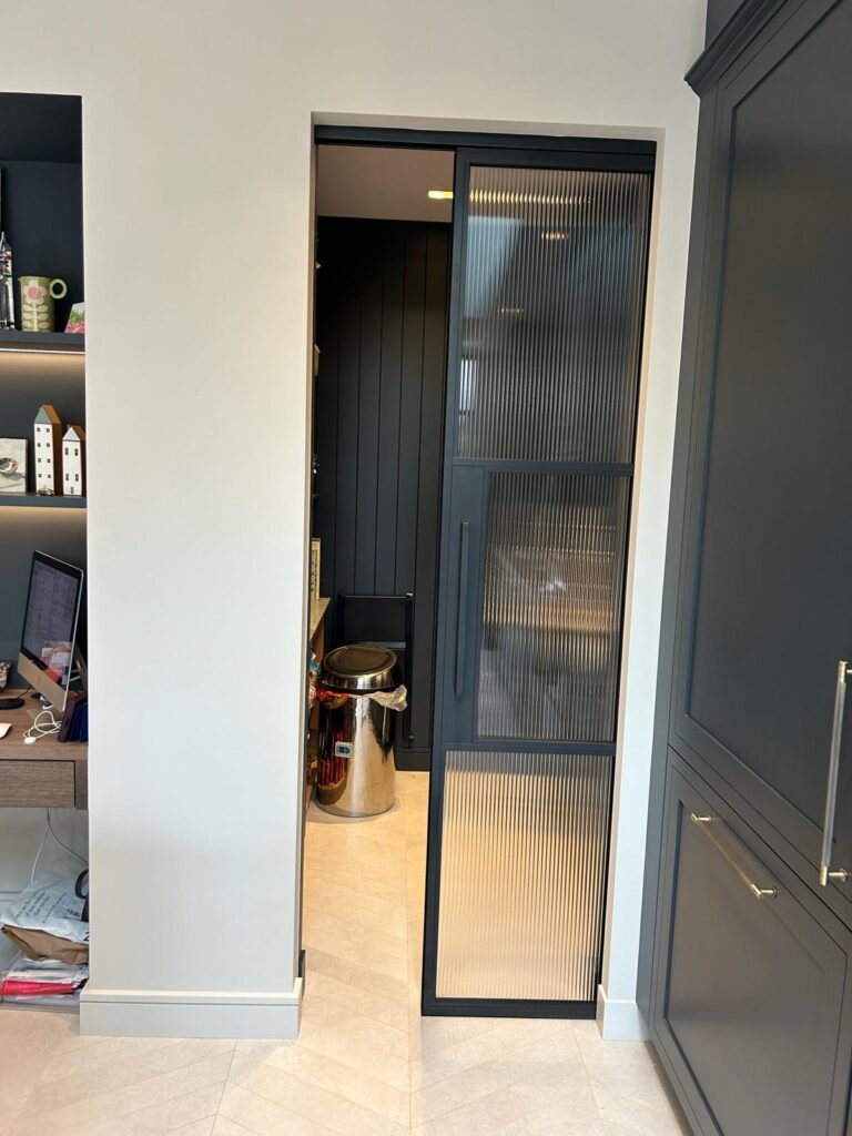 A stylish narrow passage featuring black-framed sliding doors internal with ribbed glass, providing a subtle separation.