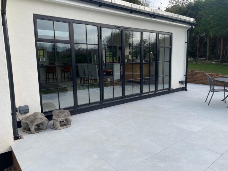 Black-framed steel doors with glass panels open onto a modern patio, seamlessly connecting the interior and exterior spaces.