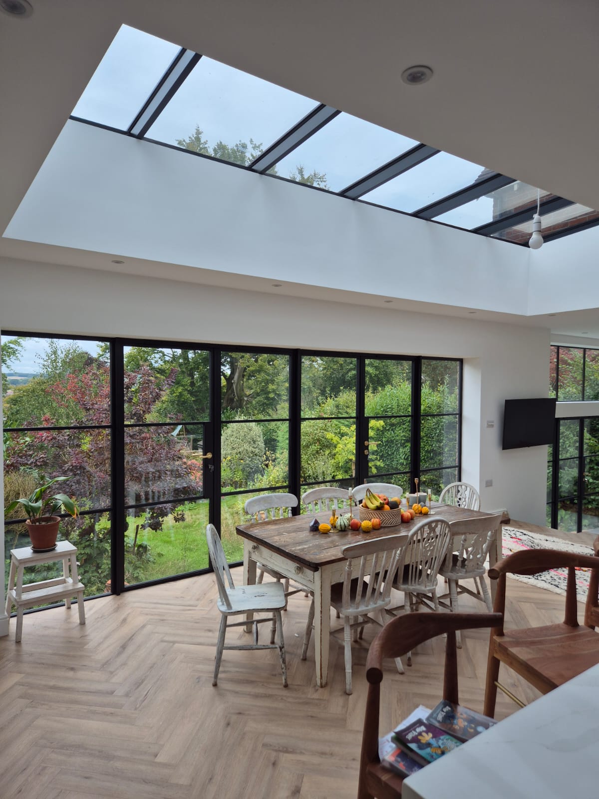 A bright dining area featuring black steel doors and floor to ceiling windows with elegant steel framed doors, offering views of a lush garden.